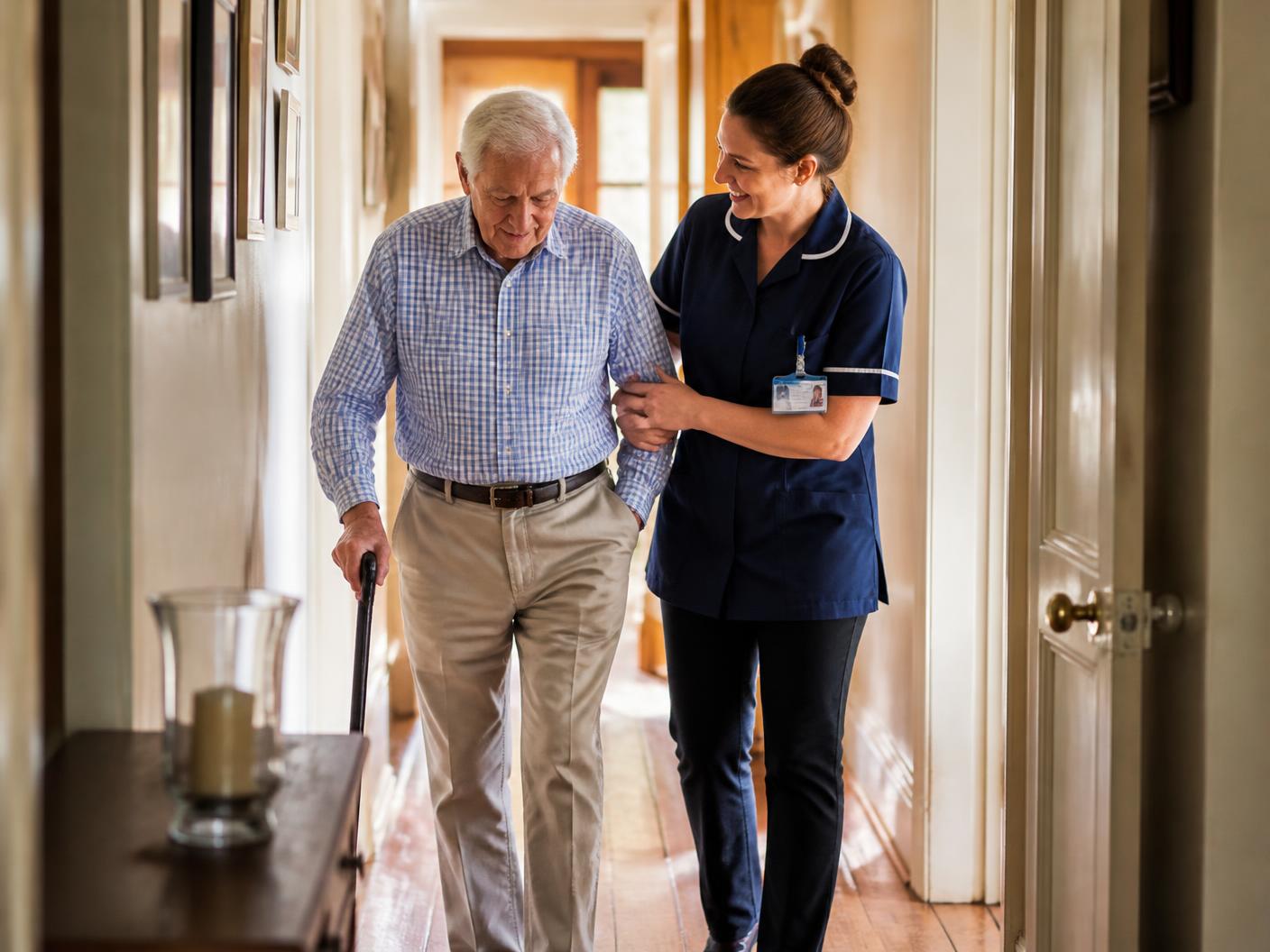 A caregiver walking arm in arm with an older man in his home